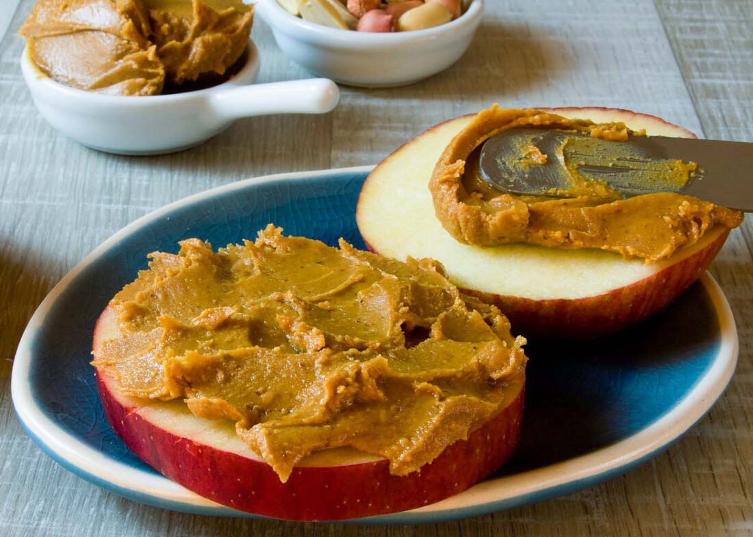 Two apple slices spread with peanut butter on a blue plate