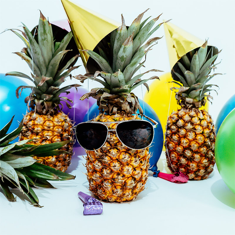 Pineapples, one wearing sunglasses, surrounded by balloons