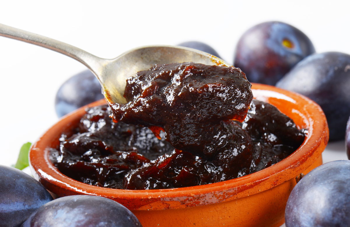 A spoon scooping up plum sauce from a bowl, surrounded by whole plums