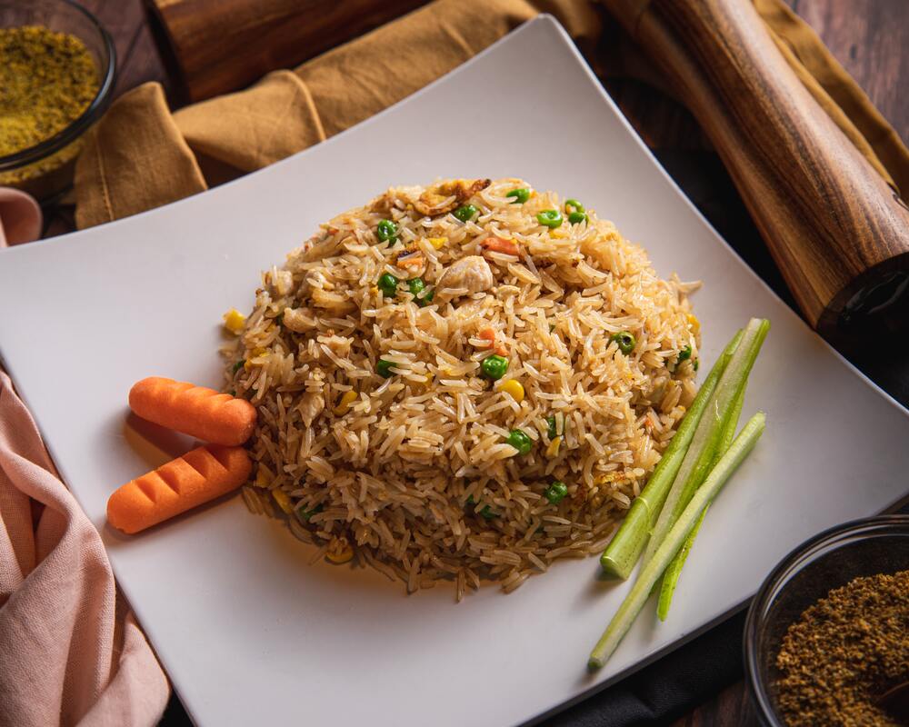Brown rice with carrots, peas, corns, and green onions on a white plate