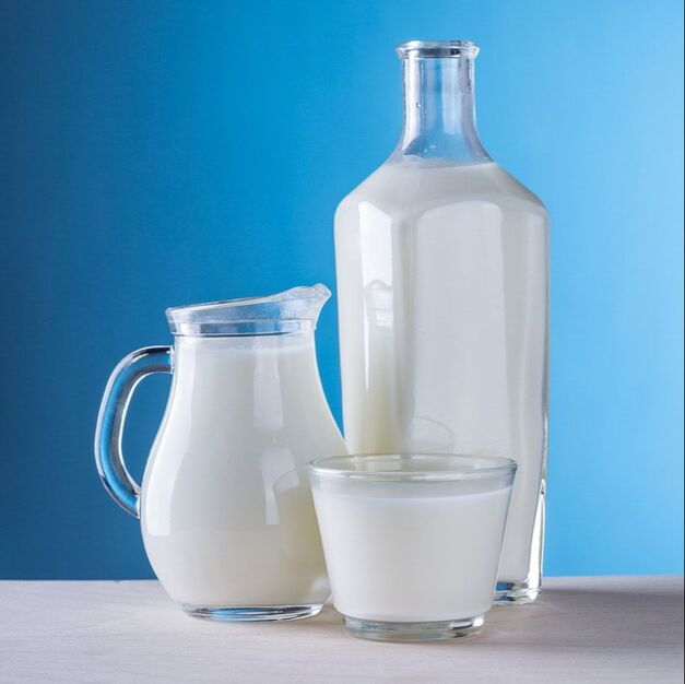 A jug of milk, pitcher of milk, and glass of milk on a grey table against a blue background