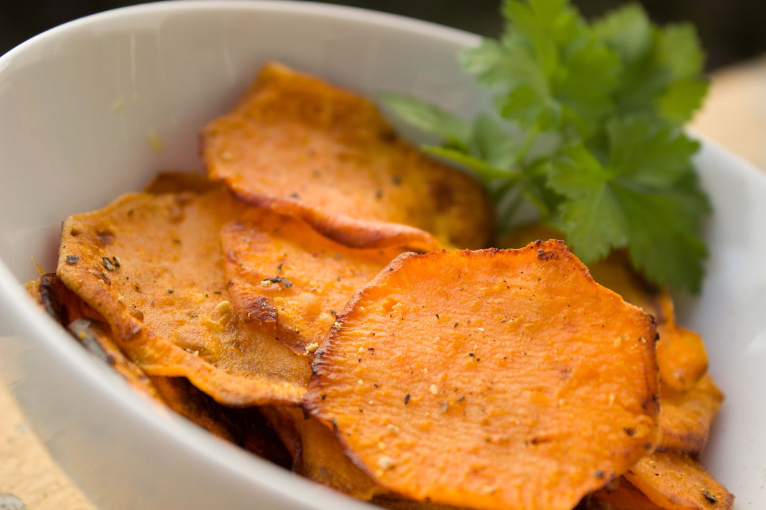 Baked sweet potato slices in a white bowl with a leafy garnish